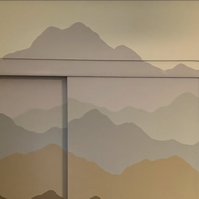 Layered mountain range mural in soft grays and sand tones wrapping a bedroom wall and closet doors