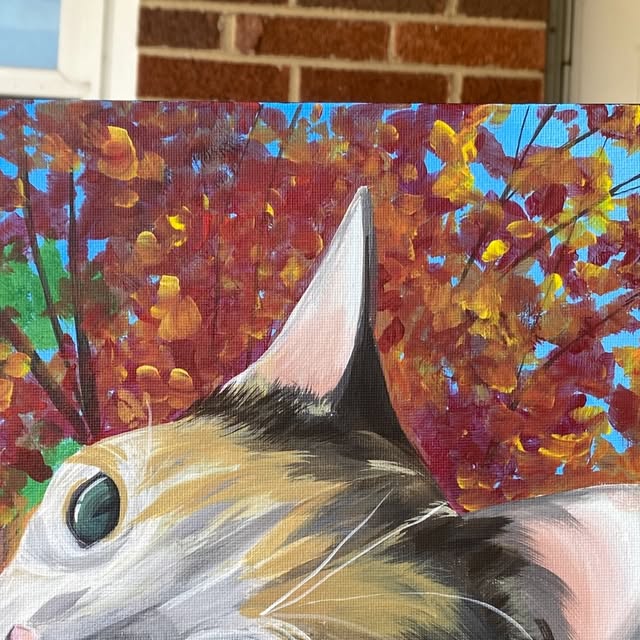 Portrait of a calico cat peeking up in front of red and gold autumn leaves
